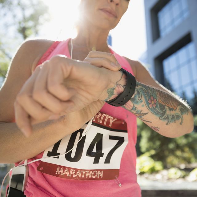 Tattooed female marathon runner checking smart watch in urban park