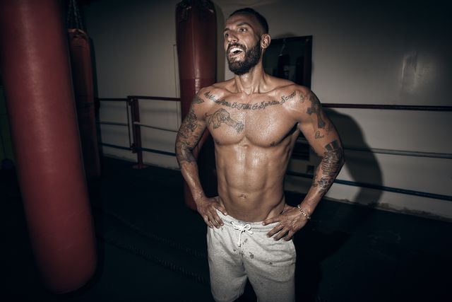 Tattooed male boxer with hands on hips laughing in gym