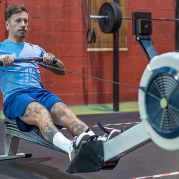 tattooed man rowing on ergometer in gym crosstraining box wearing blue sportswear
