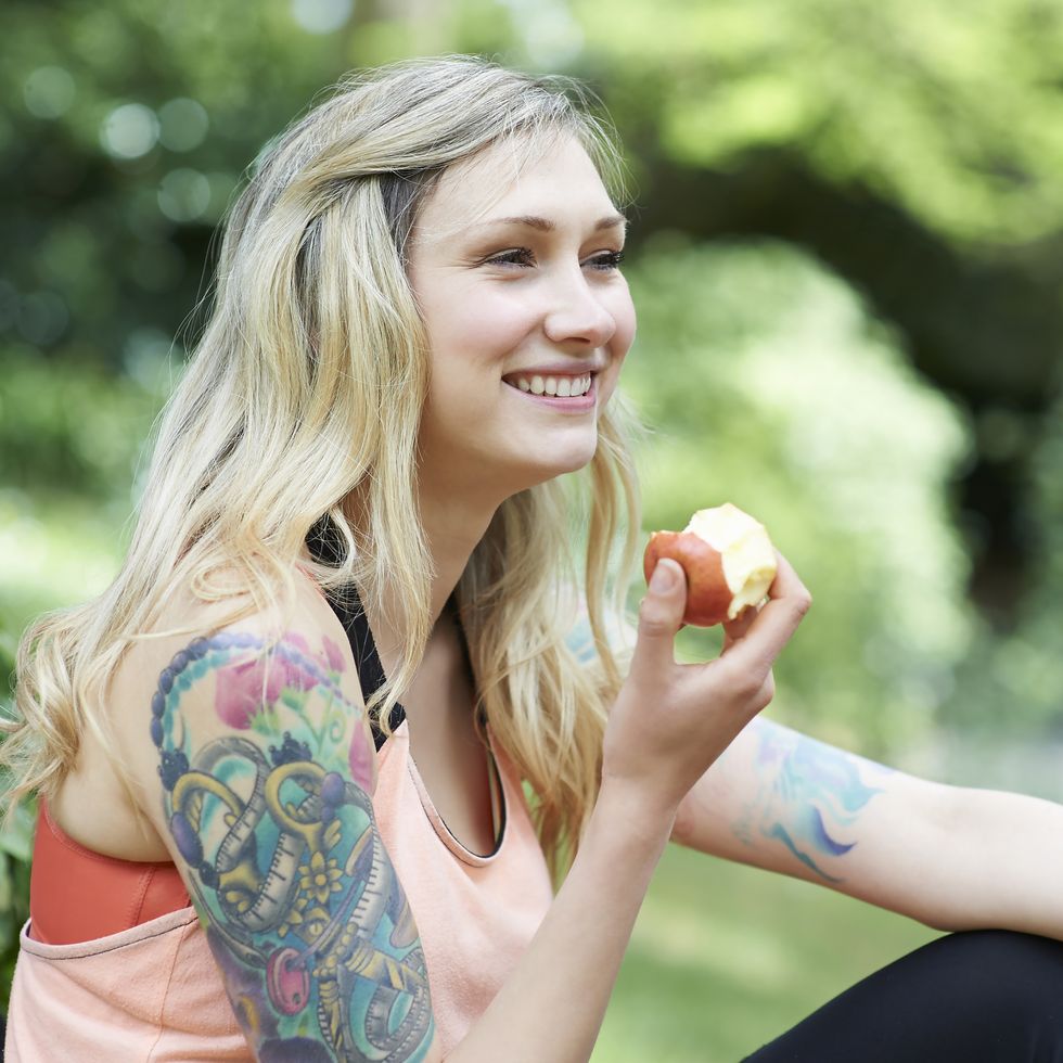 tattooed woman sitting in countryside eating apple