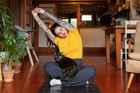 tattooed woman stretching at home with cat in lap