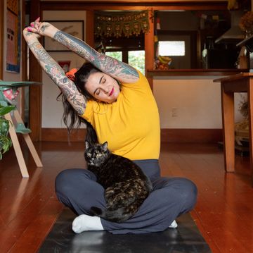 tattooed woman stretching at home with cat in lap