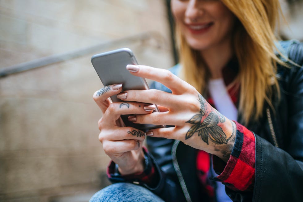 una mujer con las manos tatuadas consulta su teléfono móvil
