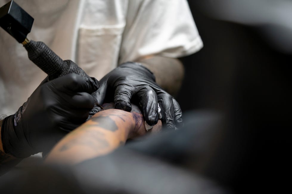 tattooist tattooing young mans arm, close up