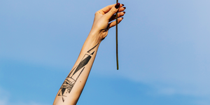 arm with tattoo holding yellow flower to the sky