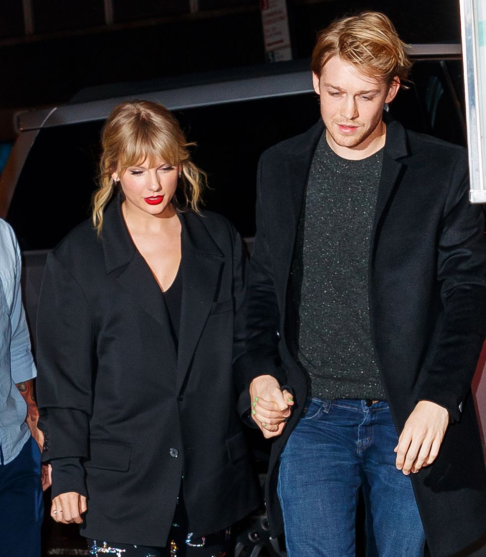 taylor swift and joe alwyn walk hand in hand and look down, both wear black coats, he also has on jeans and a gray sweater