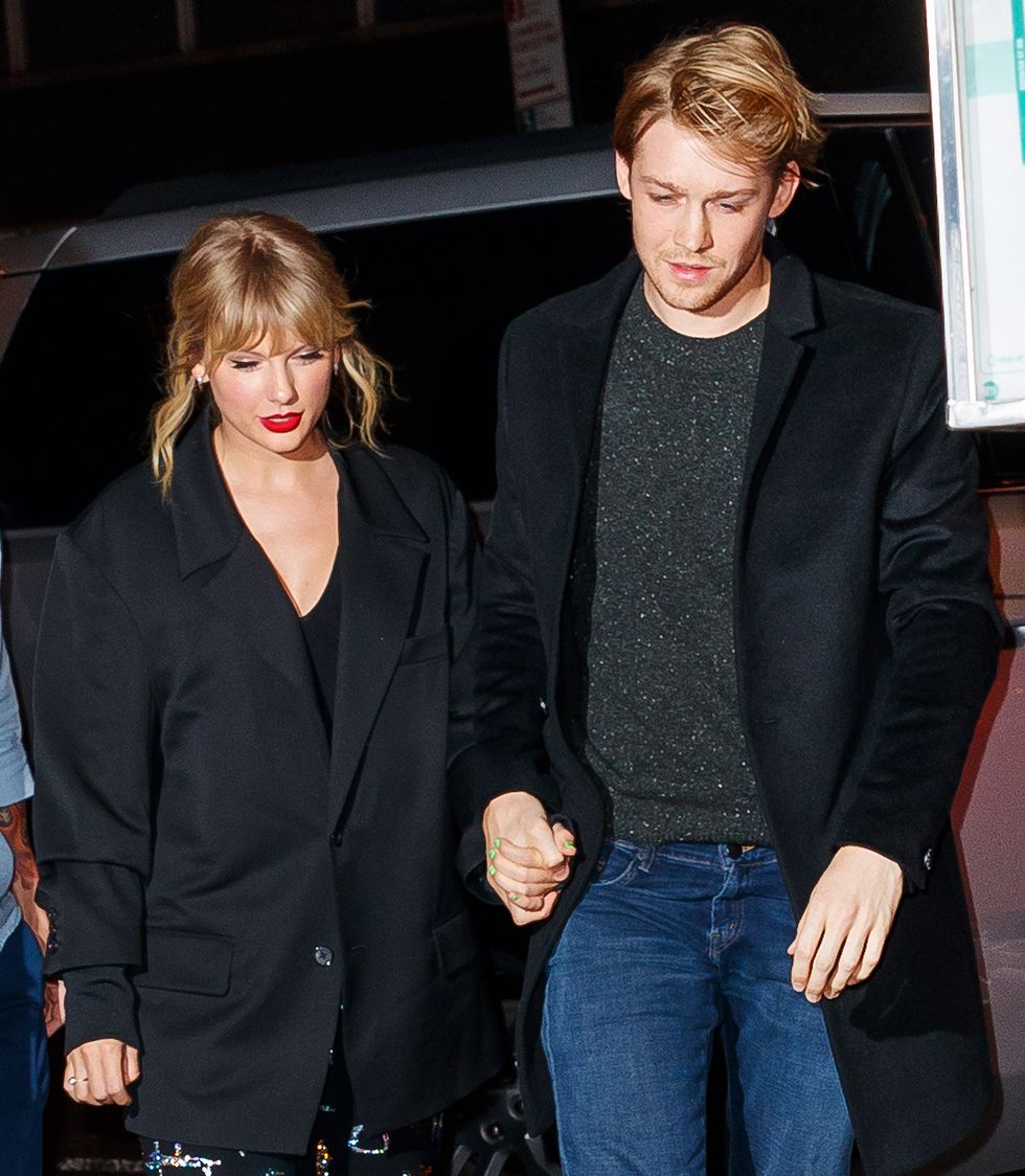 taylor swift and joe alwyn walk hand in hand and look down, both wear black coats, he also has on jeans and a gray sweater