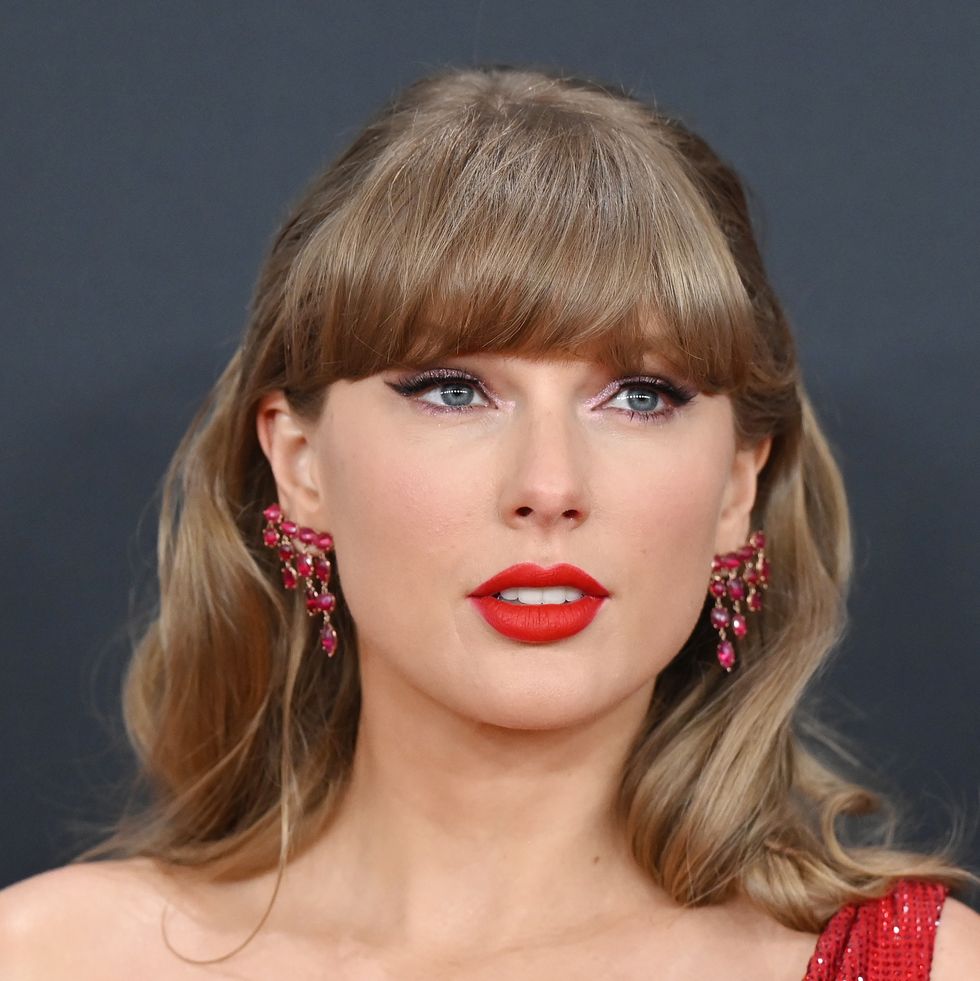 a woman looks to the right, she wears dangling ruby earrings and red lipstick