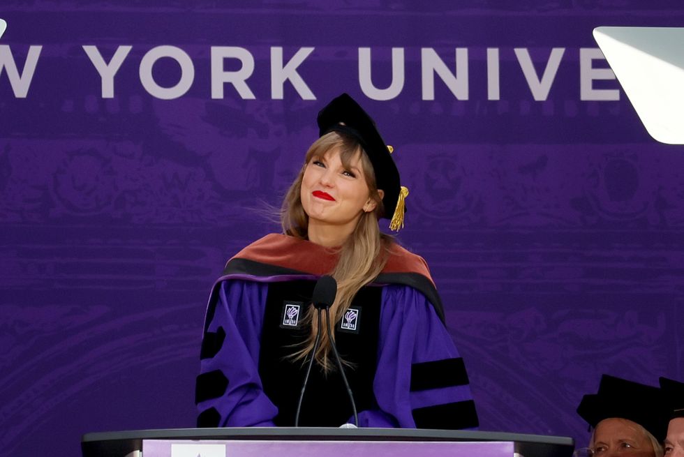 a woman in a purple and black graduation gown and cap smiles as she stands at a podium with a microphone