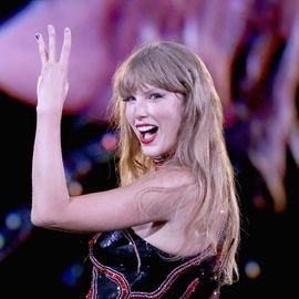 a woman smiles while looking over one shoulder and holding up three fingers un the air