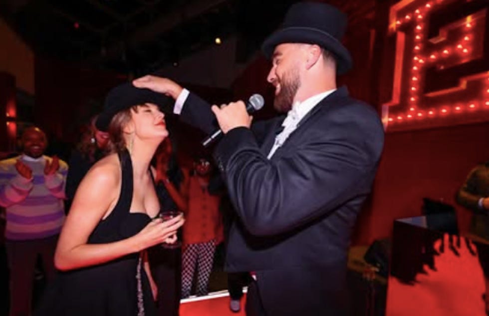 a person in a suit and top hat is interacting with another person in a party setting