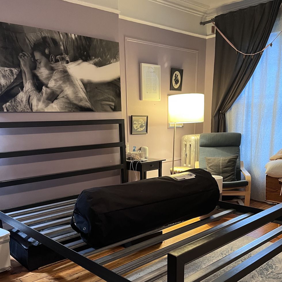 a bedroom with a black slatted bed frame and a rolled mattress sitting on top of the frame during the setup process
