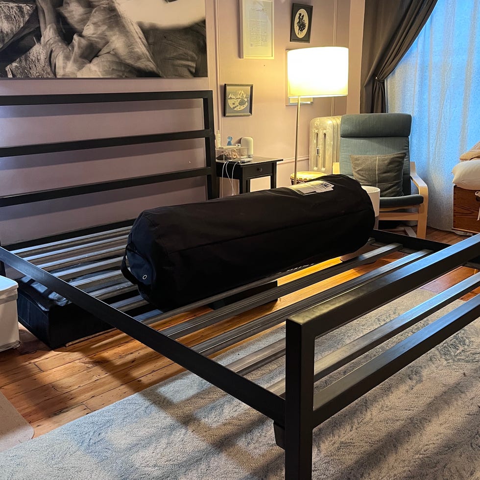 tempur-cloud review - setup process a bedroom with a black slatted bed frame and a rolled mattress sitting on top of the frame during the setup process