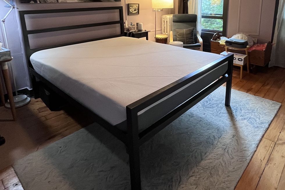 a bedroom with a black bed frame and an uncovered white tempur cloud mattress on top during the setup process