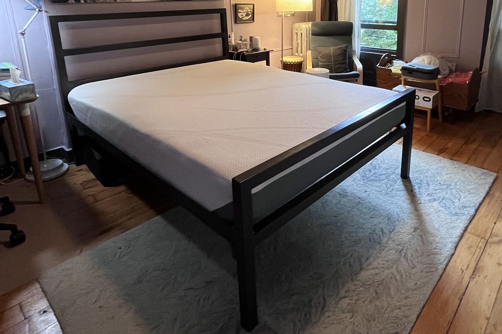a bedroom with a black bed frame and an uncovered white tempur cloud mattress on top during the setup process