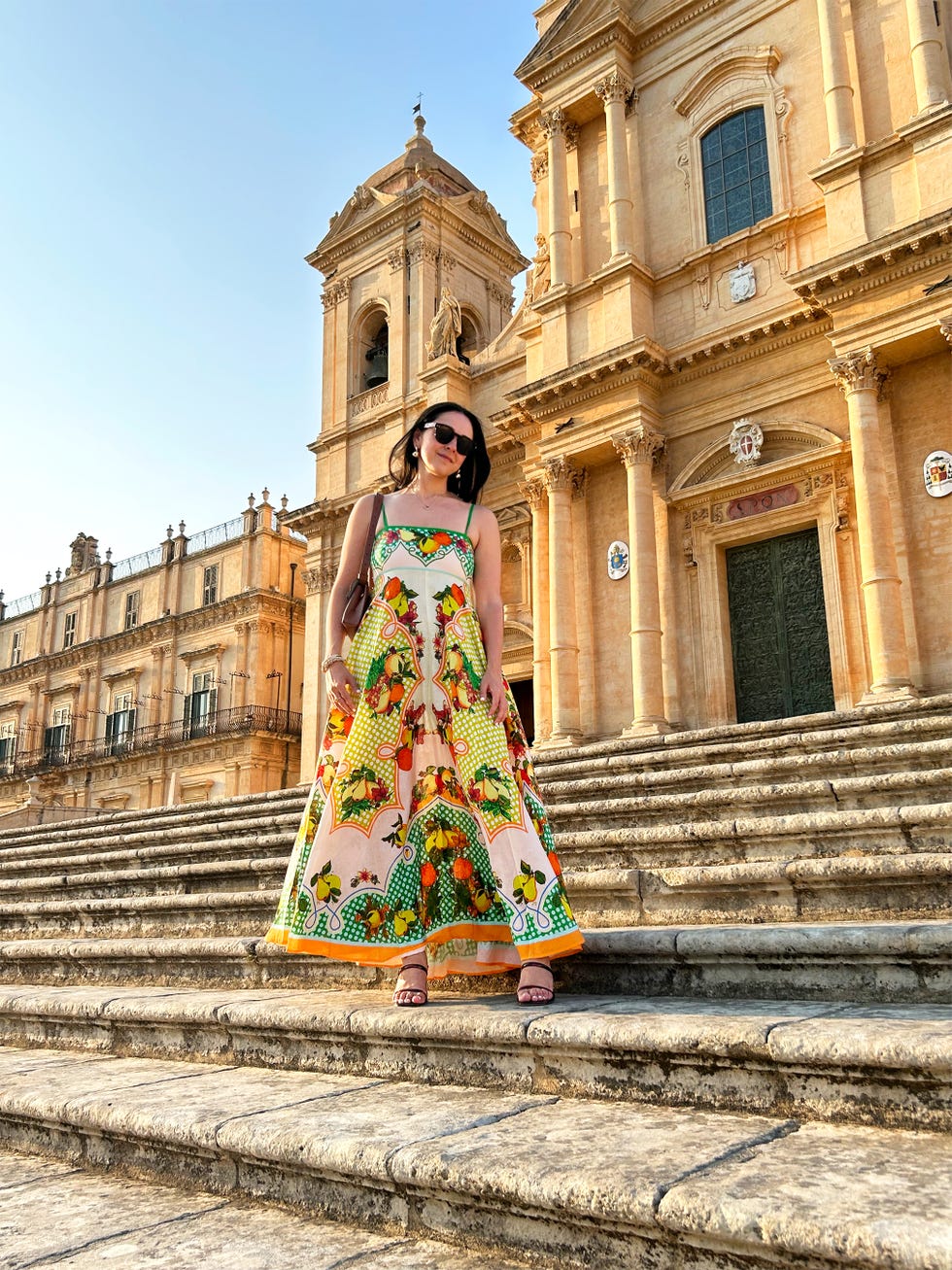 a person stands on steps outside a grand building wearing a colorful dress