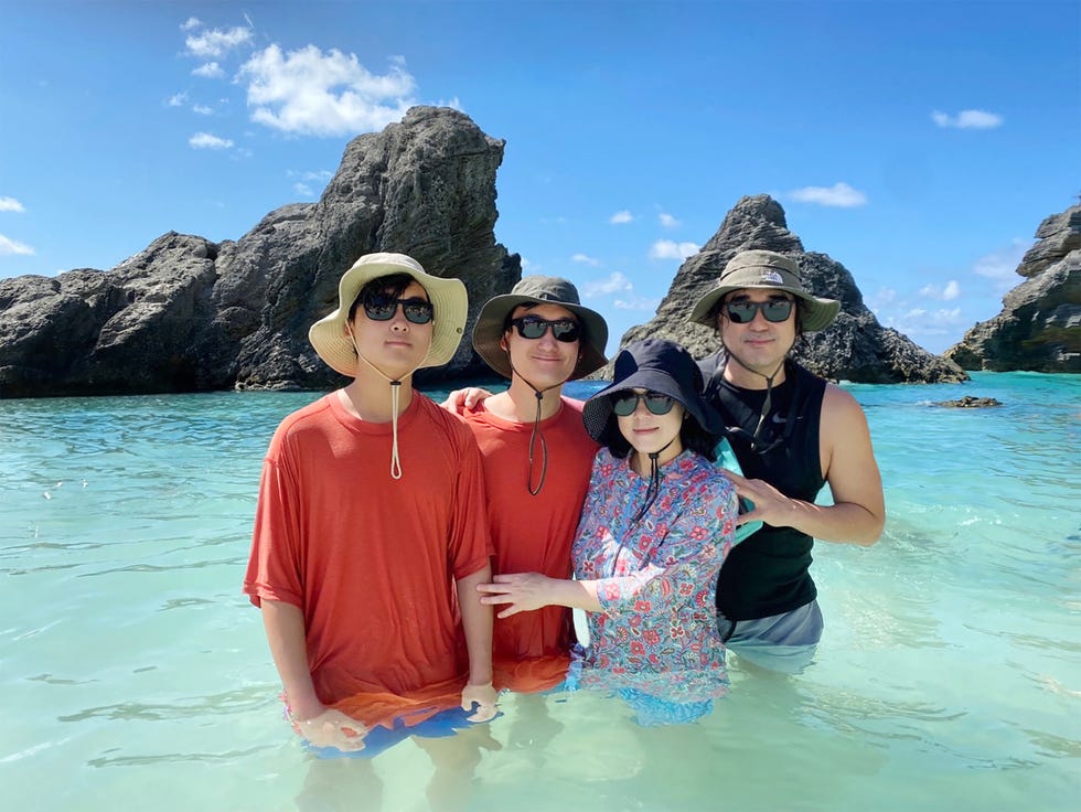 group of four people standing together in shallow water at the beach with rocky formations in the background