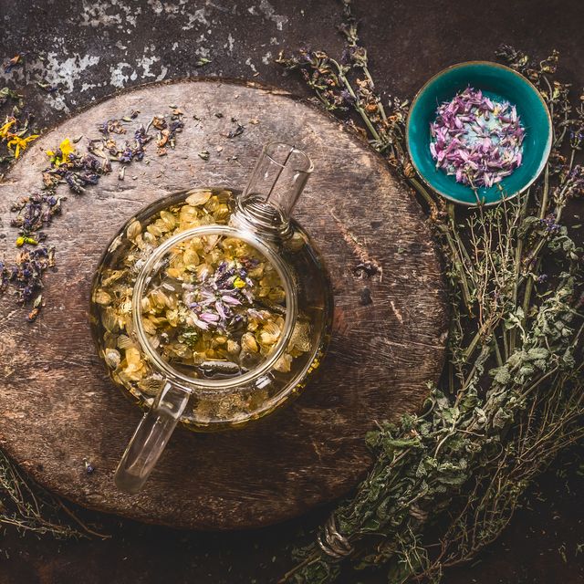 teapot with herbal tea on dark background with medicinal herbs and flowers