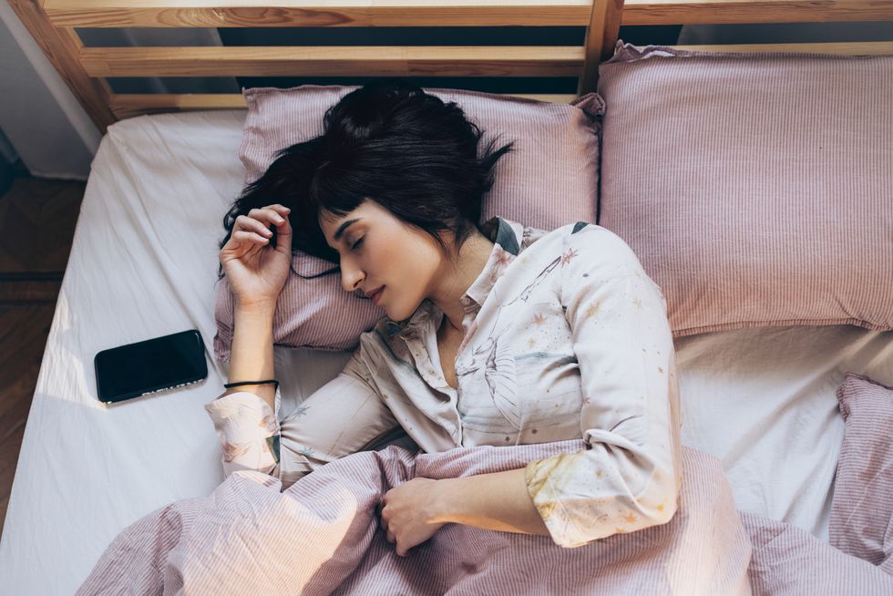 technology aided sleep woman in pyjamas listening to relaxing music on her smartphone in bed in the morning