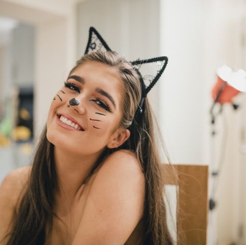 a girl with long dark hair wearing cat ears and with her face painted like a cat for halloween
