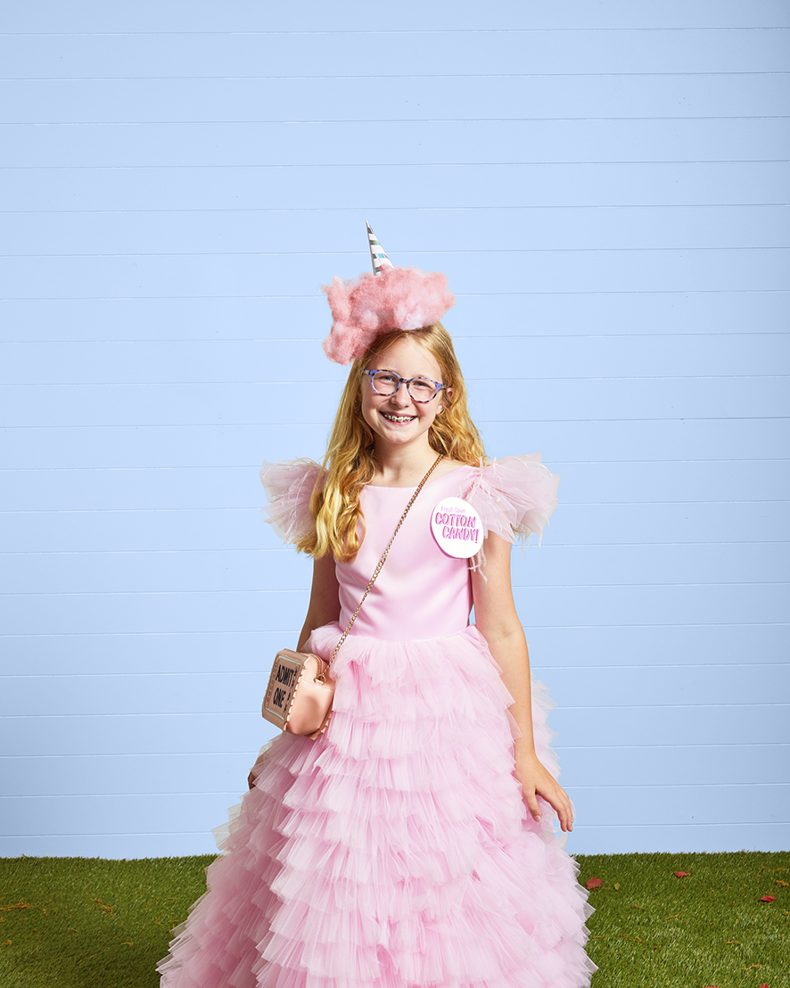 a girl dressed in a long puffy pink dress with a poof of pink cotton on her head to resemble cotton candy