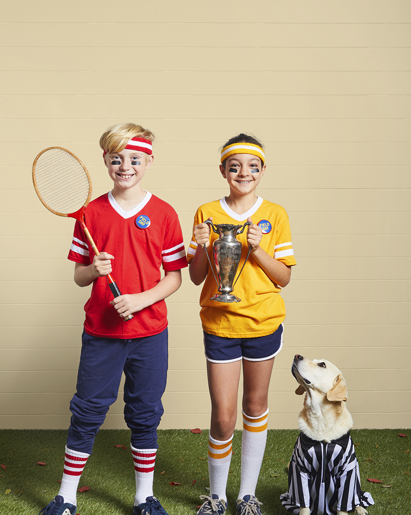 a boy and a girl and a dog dressed for field day in knee socks and sweatbands with a trophy and sports raquet