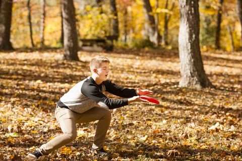 Teenage boy catching flying disc in autumn forest