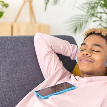 teenage boy listening to music with mobile phone and headphones while lying on a sofa at home