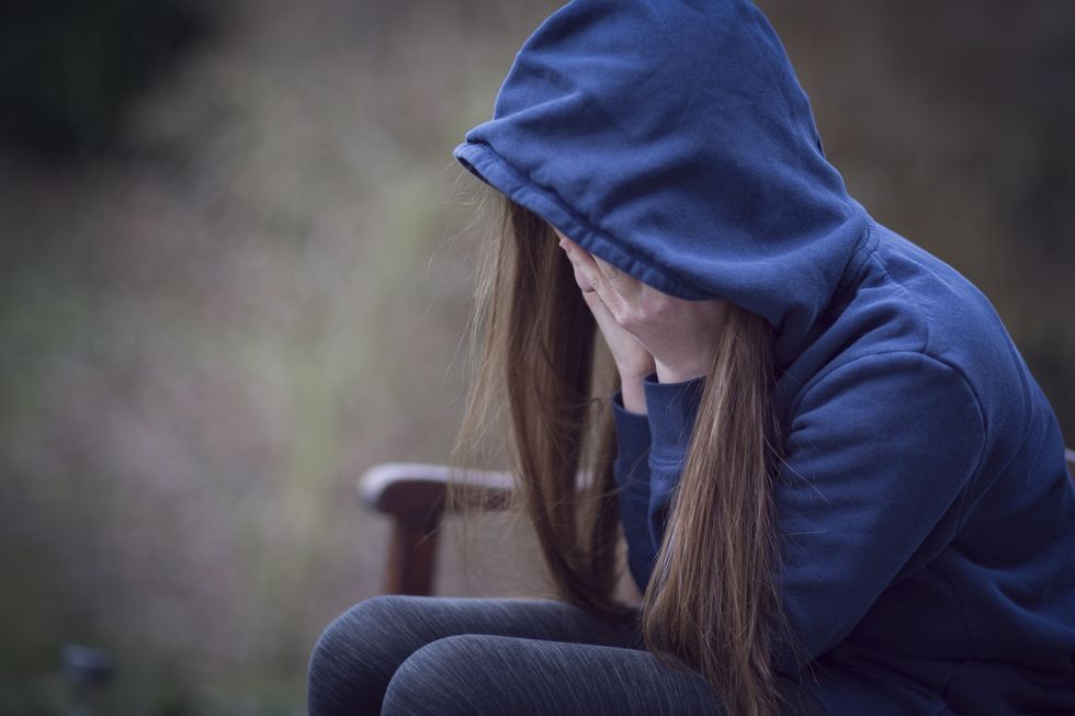 Teenage girl in hooded top, with head in hands in despair