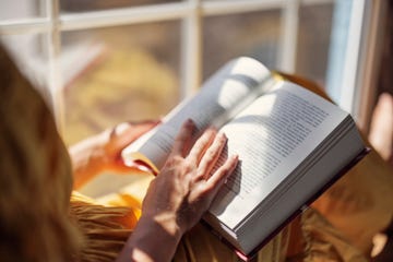 mujer sentada junto a la ventana leyendo un libro
