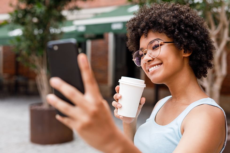 teenage girl taking selfie while holding disposable cup