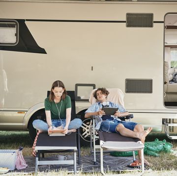 teenage siblings watching movie on digital tablet while sitting on folding chairs against motor home at campsite