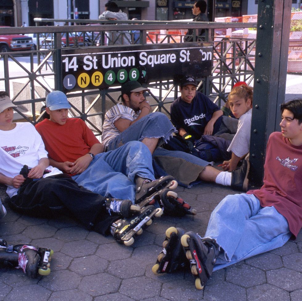 teenagers in rollerblades sitting on pavement in union square, next to subway station