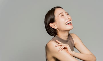 a japanese woman with bob hair is sitting sideways and smiling.