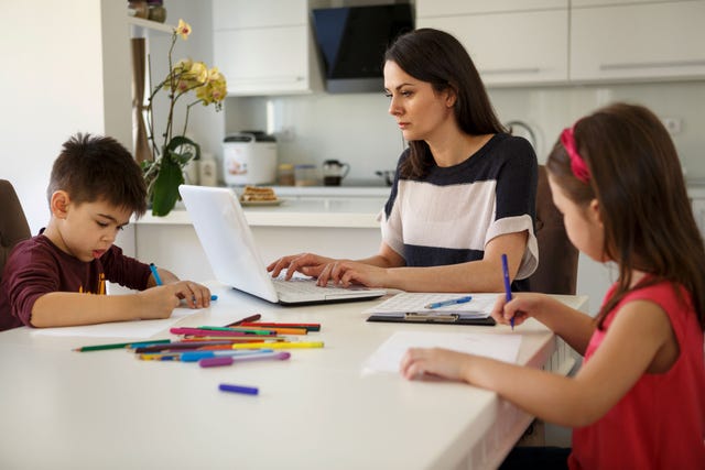 mujer teletrabajando con sus hijos al lado