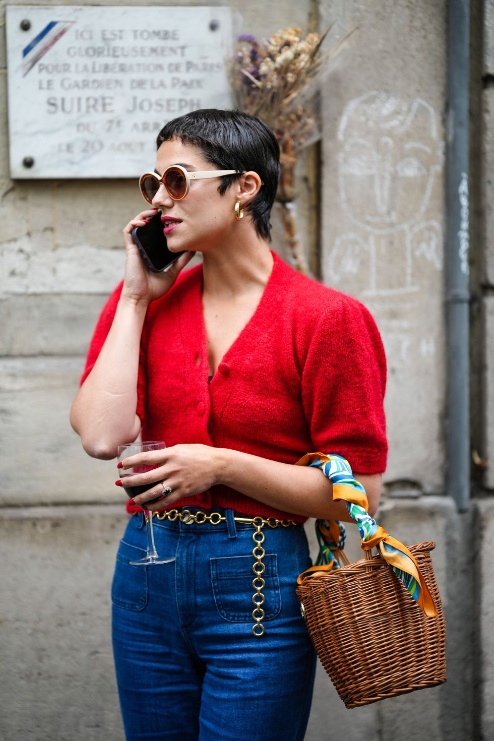 paris, france   june 25 a guest wears circle sunglasses, a red fluffy puffy short sleeves  buttoned cropped cardigan, navy blue denim wide legs pants, a brown wickers basket handbag, a green  blue  orange print pattern silk scarf, rings, a gold chain belt, outside the hermes show, during paris fashion week   menswear springsummer 2023, on june 25, 2022 in paris, france photo by edward berthelotgetty images