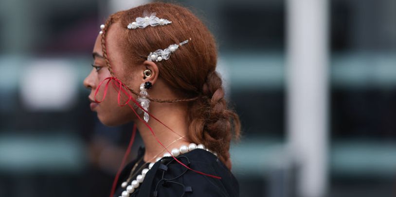 london, england september 17 a fashion week guest is seen wearing a complete simone rocha look, consitinng of an earring with gemstone ornaments and sr logo covered in rhinestones another smaler earring with peals and transparent ornaments the matching hair clips a black dress with laced up details, puffy sleeves, round high neckline, mesh parts and several red bows a creme white egg shaped bag with pearl strap during london fashion week september 2023 before the simone rocha show on september 17, 2023 in london, england photo by jeremy moellergetty images