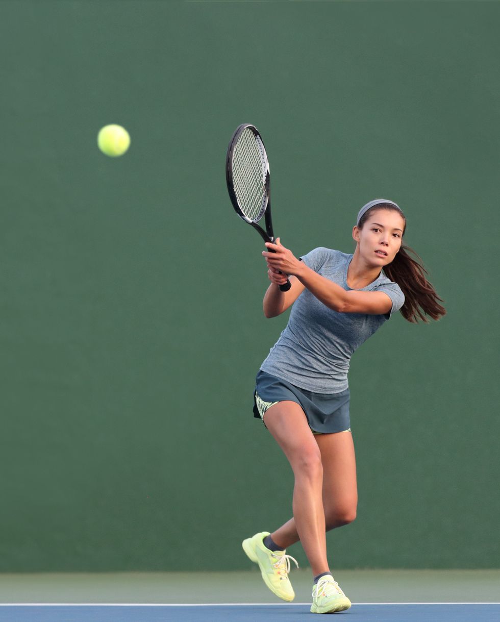 tennis playing woman hitting ball on green hard courtasian athlete girl returning serve with racket wearing skort and shoes