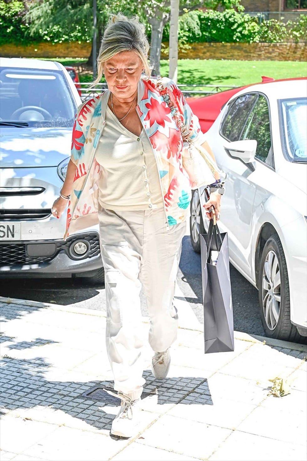 a woman carrying a shopping bag dressed in a colorful floral shirt and light trousers walking on a sidewalk