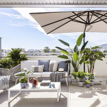 terraza con zona de estar y comedor en blanco y azul con sombrilla