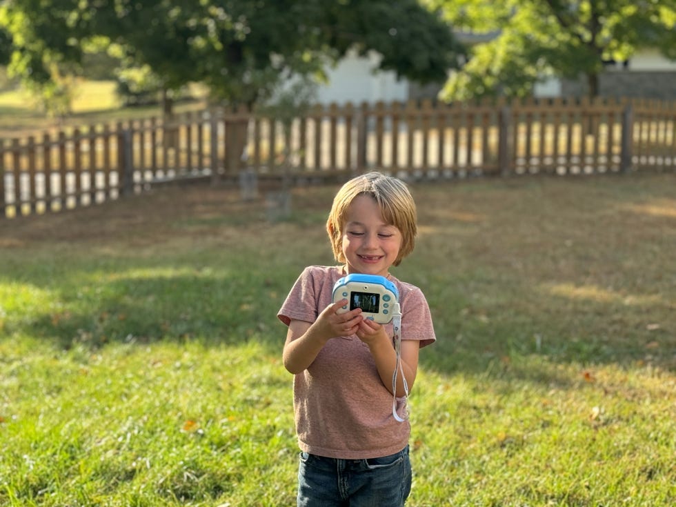 a boy holds a blue and white kids camera to take a selfie, part of a good housekeeping test of the best kids cameras