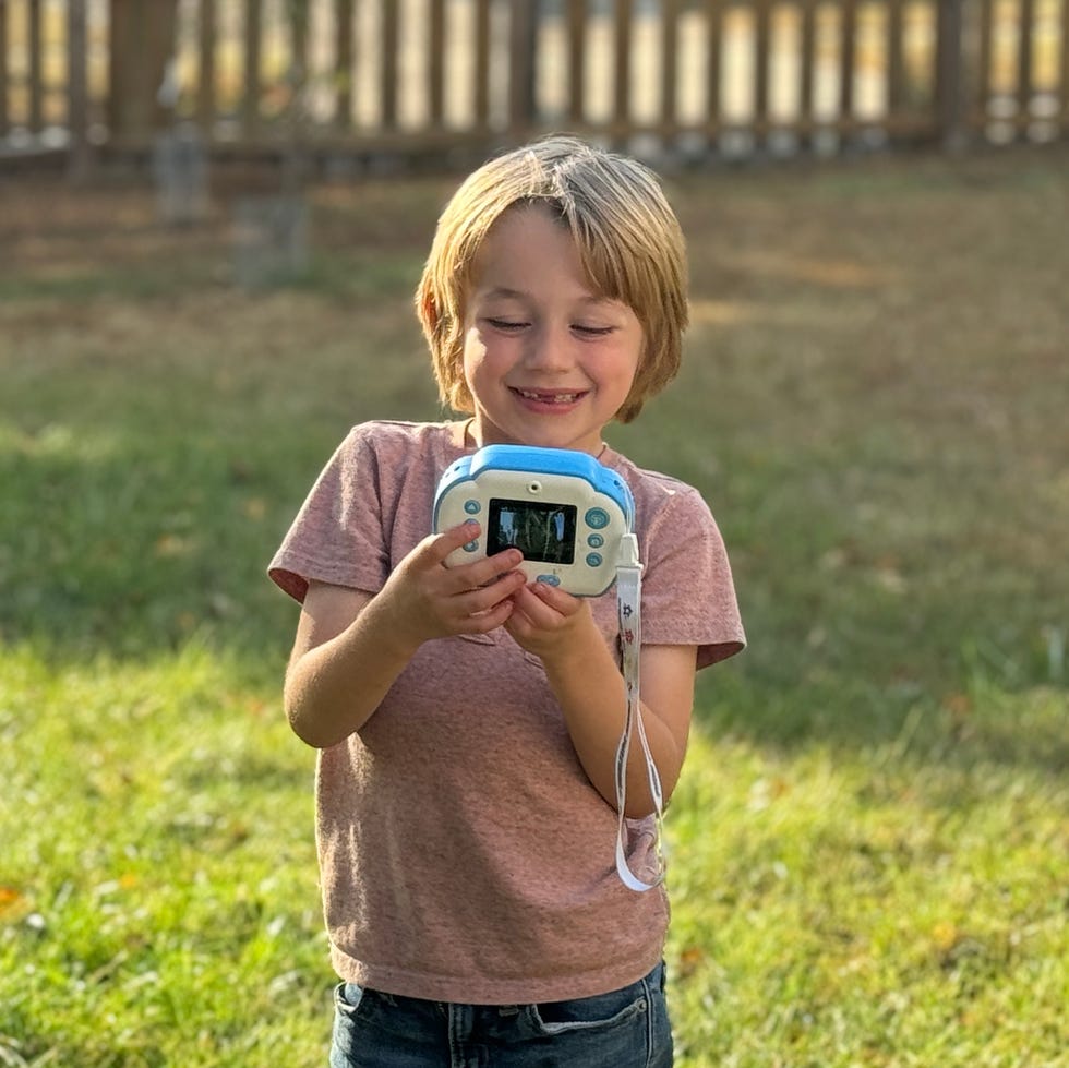 testing the paw patrol kids camera in the outdoors a boy holds a blue and white kids camera to take a selfie, part of a good housekeeping test of the best kids cameras