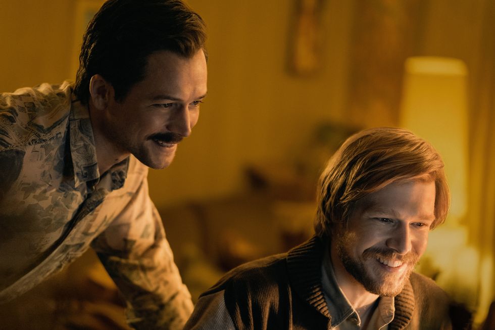 a still from the film ﻿tetris﻿, with actors ﻿taron egerton and nikita efremov looking down at something off screen and smiling