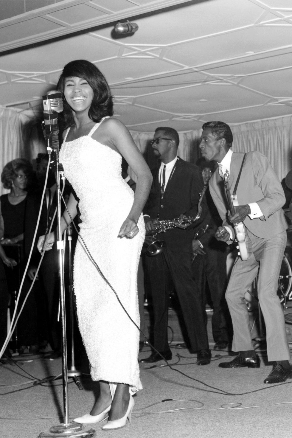 tina turner singing at a microphone, musicians play behind her