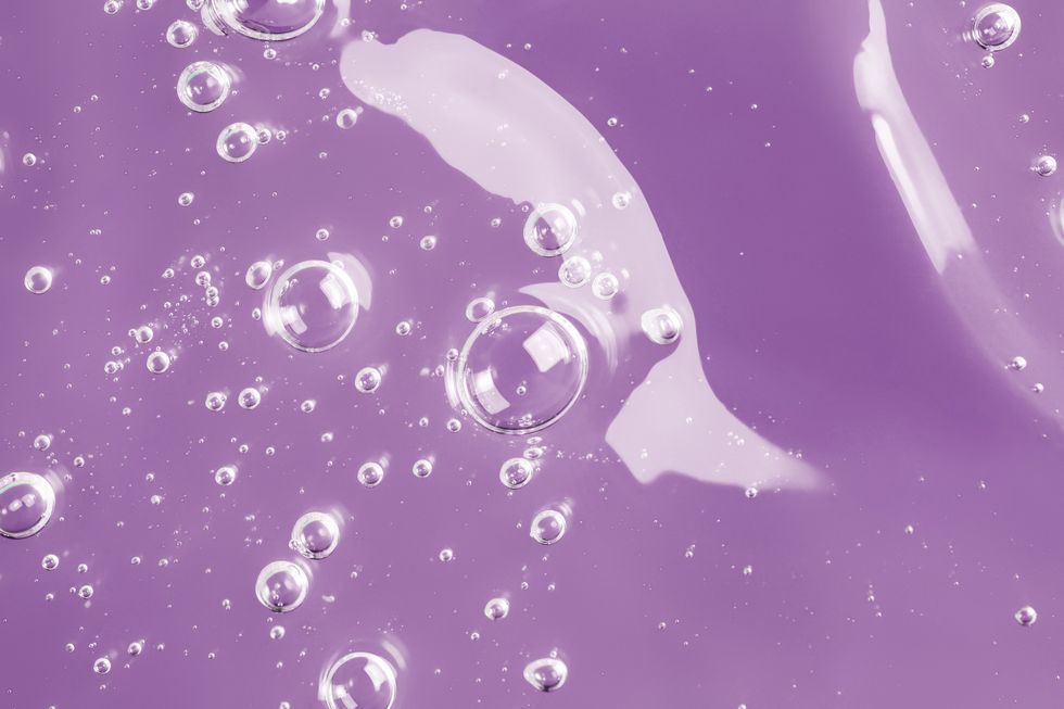 texture of organic transparent gel with many air bubbles smudged on bright purple monochrome background concept of skin moisturizing or prevention covid 19 during pandemic close up and flat lay style