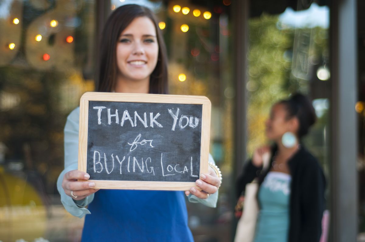 woman holding a sign that says thank you for buying local
