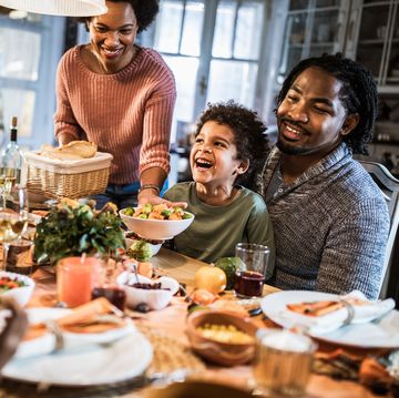 happy black mother serving dish to her family during thanksgiving meal at dining table