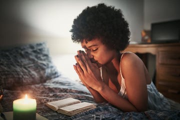 woman prays next to book and candlelight