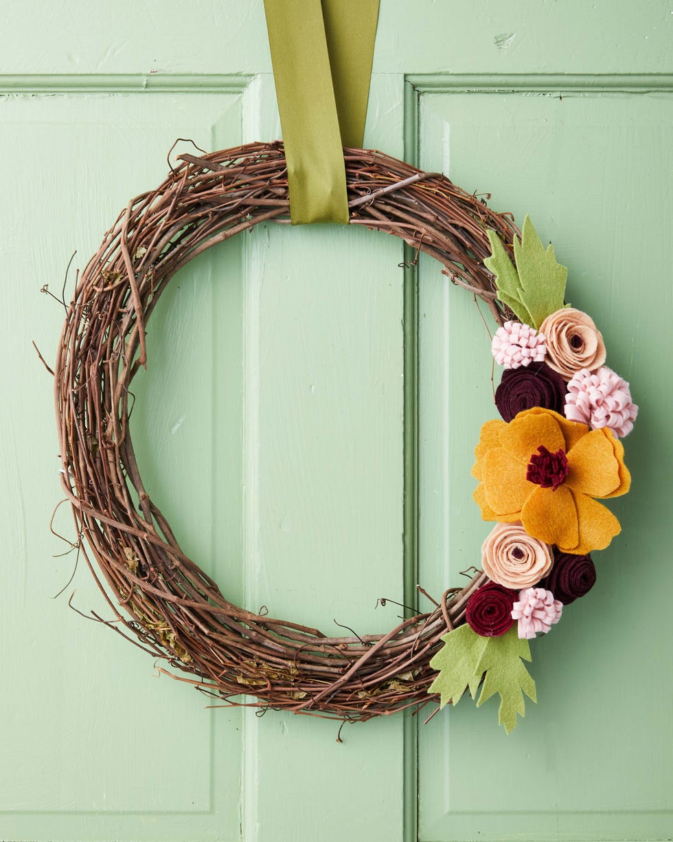 wreath made from a grapevine wreath form topped with felt flowers displayed on a green door