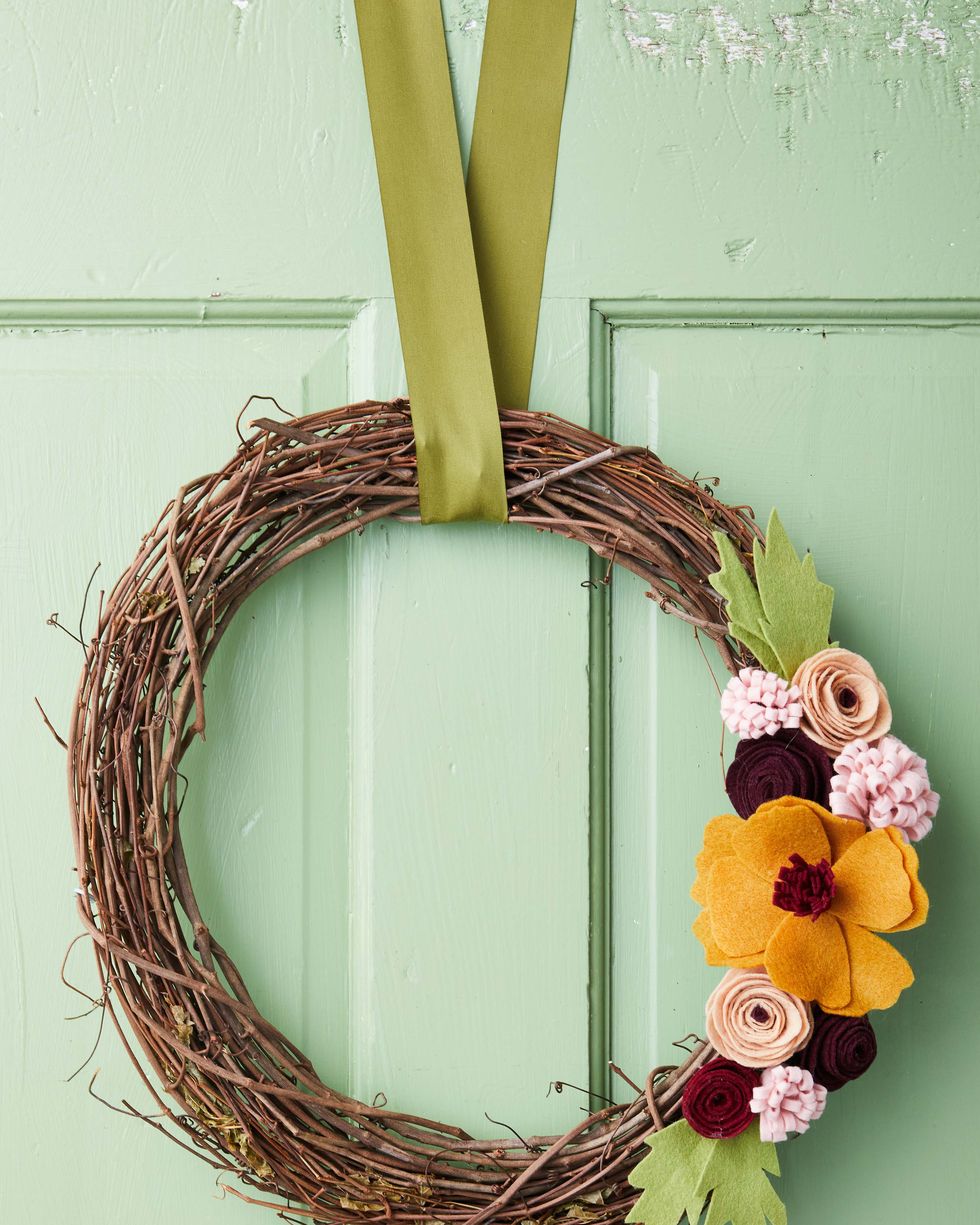 grapevine wreath topped with felt flowers and leaves hung on a light green door